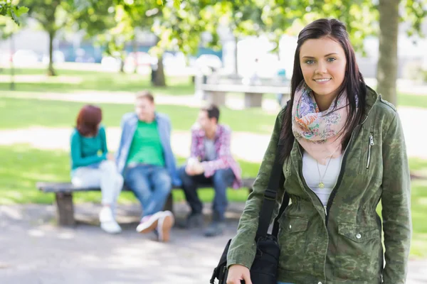 Chica universitaria sonriendo con los estudiantes borrosos en el parque — Foto de Stock