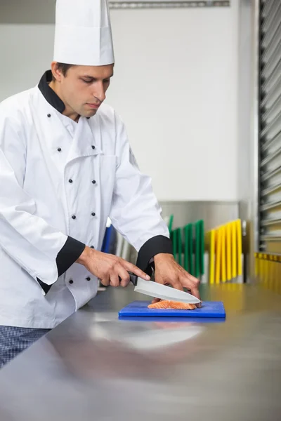 Chef sério cortando salmão cru com faca na placa de corte azul — Fotografia de Stock