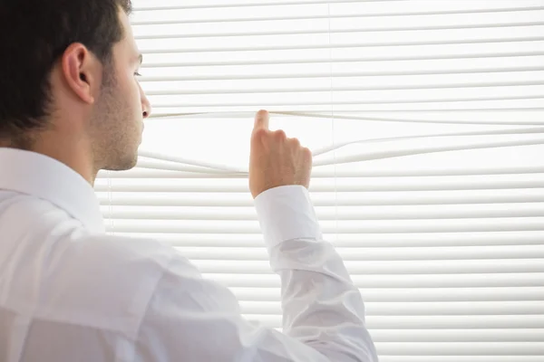 Vista trasera de hombre de negocios guapo espiando a través de persiana enrollable — Foto de Stock