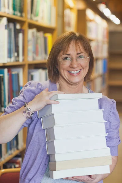 Счастливая библиотекарша с грудой книг в библиотеке — стоковое фото