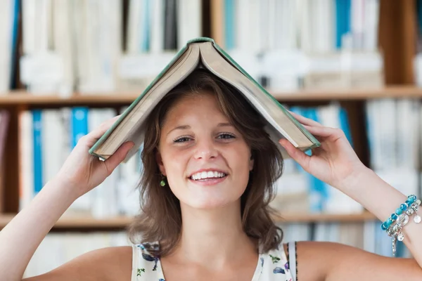 Studentka drží knihu nad hlavou v knihovně — Stock fotografie