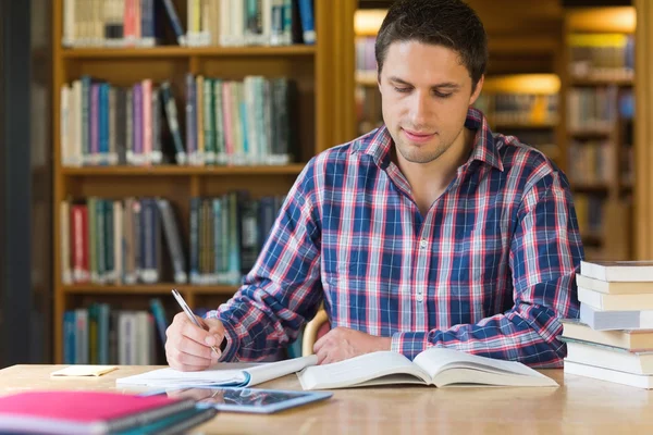 Manlig student skriva noter på skrivbord i biblioteket — Stockfoto