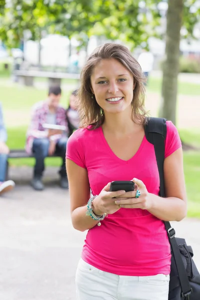 Mensajería de texto de chica universitaria con estudiantes borrosos en el parque —  Fotos de Stock