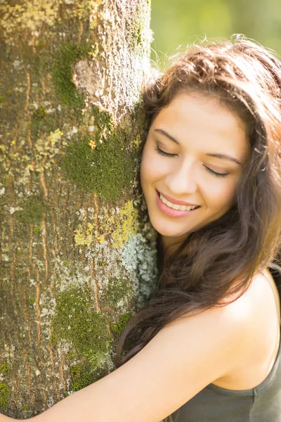 Casual morena sonriente abrazando un árbol con los ojos cerrados — Foto de Stock
