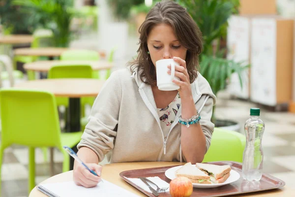 Student doing homework and having breakfast in cafeteria — Stock Photo, Image