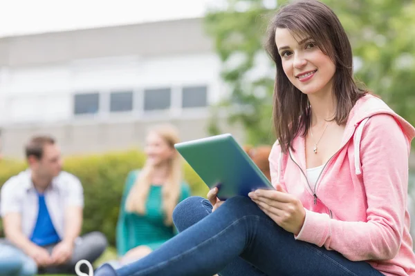 Sorrindo menina da faculdade usando tablet PC com estudantes no parque — Fotografia de Stock