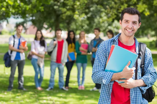 College boy håller böcker med suddiga studenter i park — Stockfoto