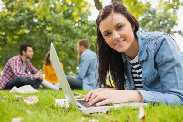 Donna sorridente che usa il computer portatile con altri studenti nel parco — Foto Stock