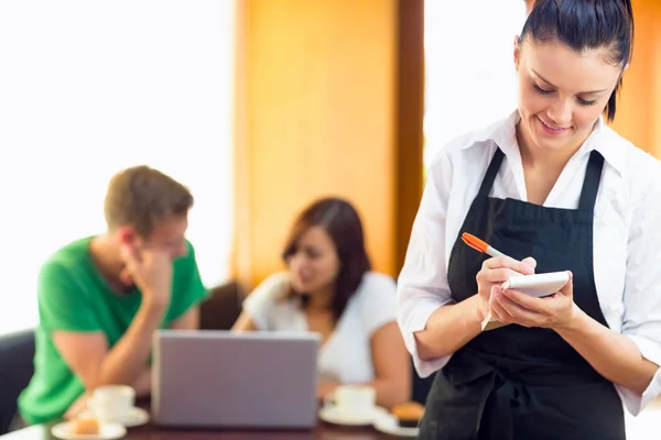 Serveerster schrijven een order met studenten met behulp van laptop op koffie — Stockfoto