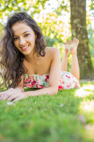 Stylový veselá brunetka ležící na trávníku při pohledu na fotoaparát — Stock fotografie