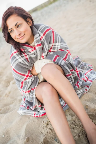 Улыбающаяся женщина, покрытая одеялом на пляже — стоковое фото