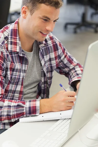 Guapo estudiante feliz usando la computadora tomando notas — Foto de Stock