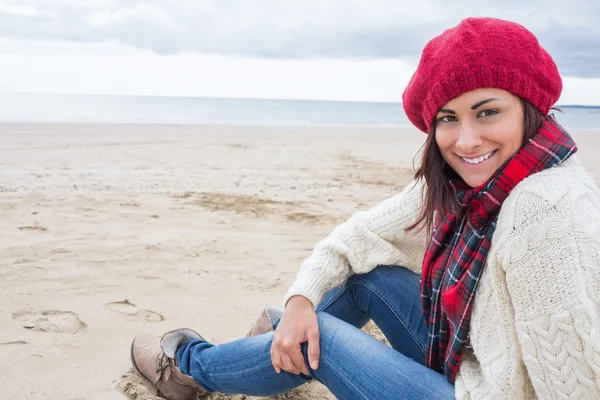 Femme souriante dans des vêtements chauds élégants assis sur la plage — Photo