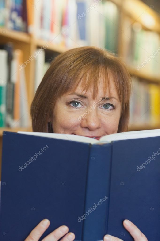 Content mature woman sitting in library holding a book Stock Photo by