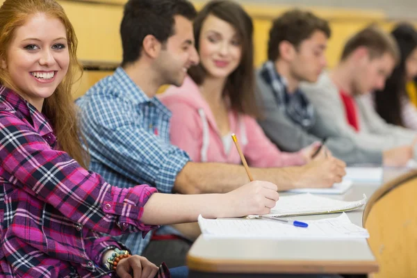 Leende kvinna med andra studenter skriva noter på föreläsningssal — Stockfoto