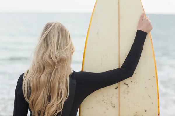 Achteraanzicht van een blonde in nat pak met surfboard op strand — Stockfoto
