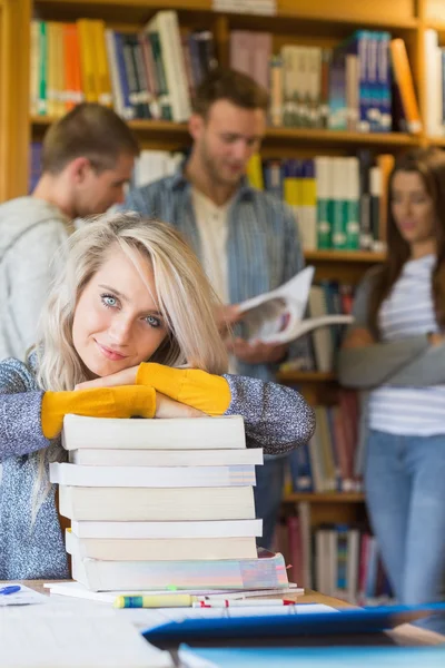 Kvinnlig student med trave böcker medan andra i bakgrunden på bibliotek — Stockfoto