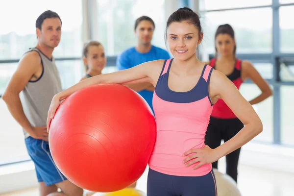 Istruttore che tiene palla esercizio con classe di fitness in background — Foto Stock