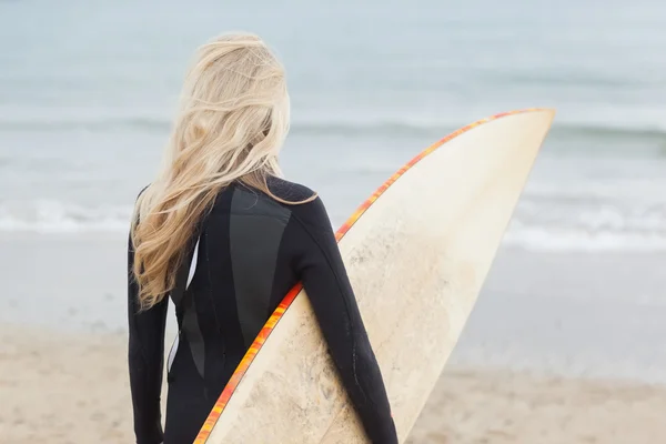 Widok z tyłu kobiety w kombinezonie trzymając deskę surfingową na plaży — Zdjęcie stockowe