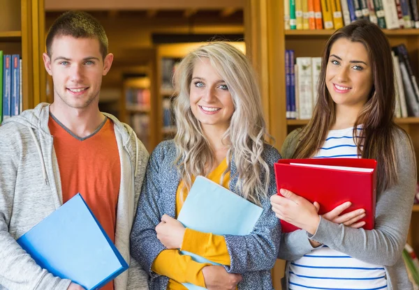 Studenti con cartelle in piedi contro libreria in biblioteca — Foto Stock