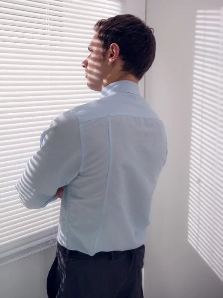 Бизнесмен подглядывает через жалюзи в офисе — стоковое фото