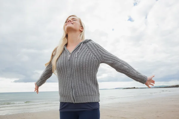 Женщина в сером трикотажном пиджаке вытягивает руки на пляже — стоковое фото