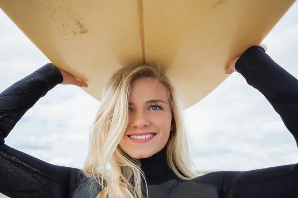 Smiling woman in wet suit holding surfboard over head — Stock Photo, Image