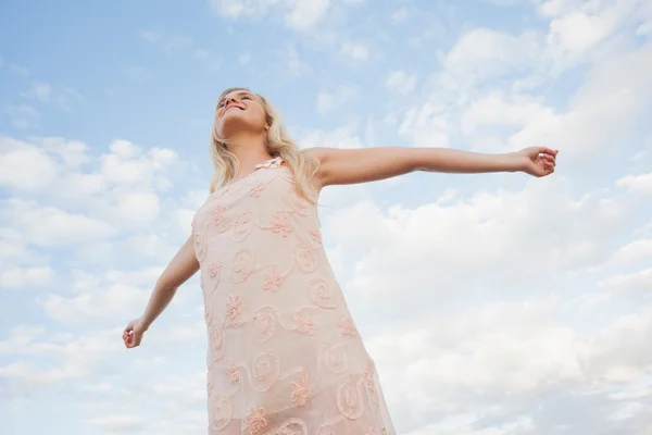 Jonge vrouw in de zomer jurk uitrekkende wapens tegen hemel — Stockfoto