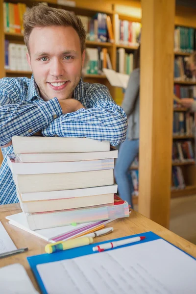 Mužský student s Stoh knih, zatímco jiné pozadí v knihovně — Stock fotografie