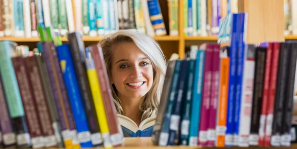 Glimlachend vrouwelijke student lezing boek in de bibliotheek — Stockfoto