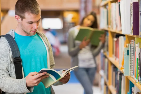 Twee jonge studenten door boekenplank in de bibliotheek — Stockfoto