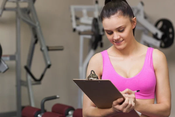 Female trainer writing on clipboard in gym — Stock Photo, Image