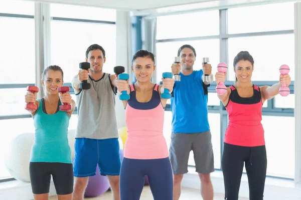 People lifting dumbbell weights with trainer in gym — Stock Photo, Image