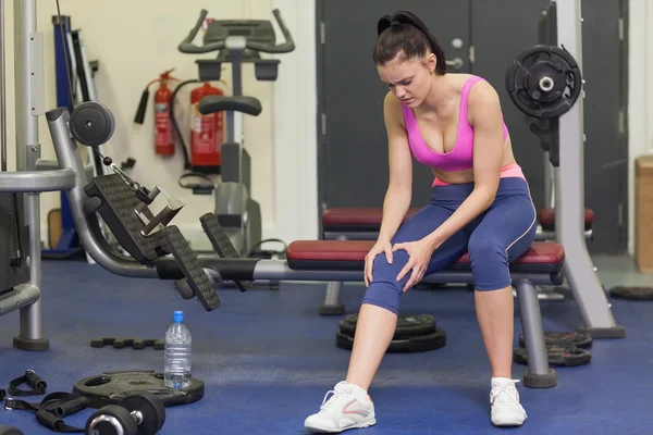 Healthy woman with an injured knee sitting in gym — Stock Photo, Image