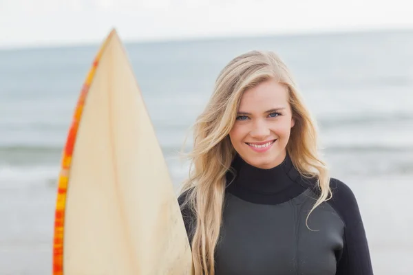 Donna sorridente in muta che tiene la tavola da surf in spiaggia — Foto Stock