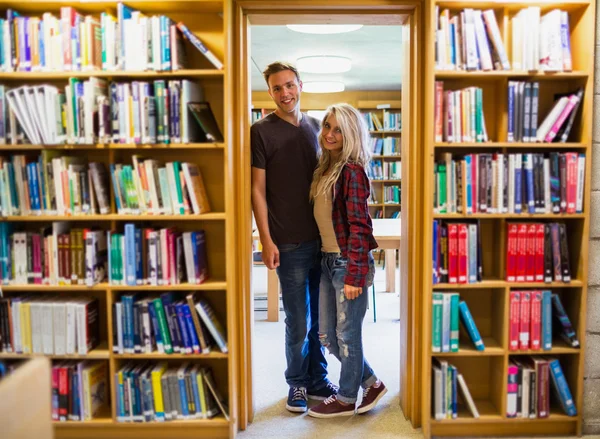 Estudantes em pé junto à estante da biblioteca — Fotografia de Stock