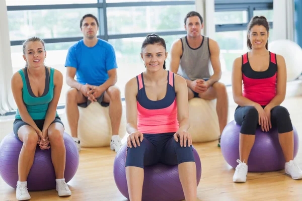 Lächelnde Menschen auf Gymnastikbällen in der hellen Turnhalle — Stockfoto