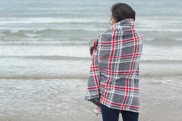 Bakifrån av kvinna täckt med filt ute till havs på stranden — Stockfoto