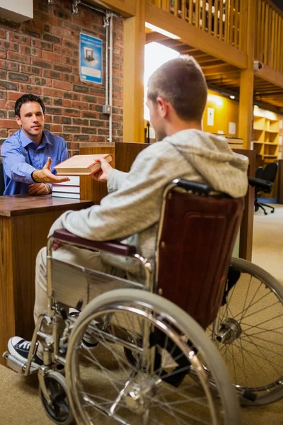 Студент в инвалидной коляске у стойки библиотеки — стоковое фото