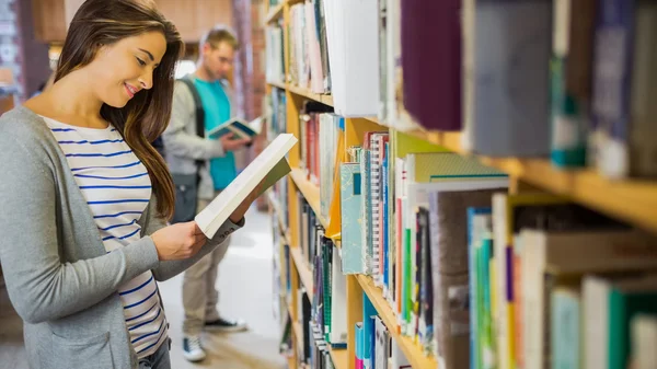 Twee jonge studenten door boekenplank in de bibliotheek — Stockfoto