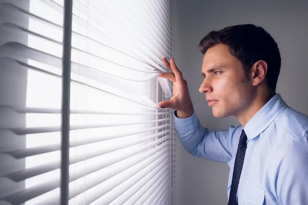 Businessman peeking through blinds in office — Stock Photo, Image