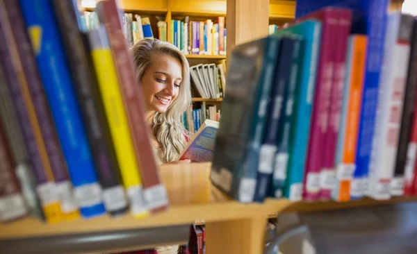 Smiling female student reading book in the library — Stock Photo, Image