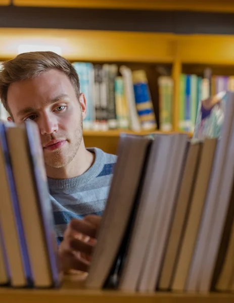 Manlig student att välja bok i biblioteket — Stockfoto