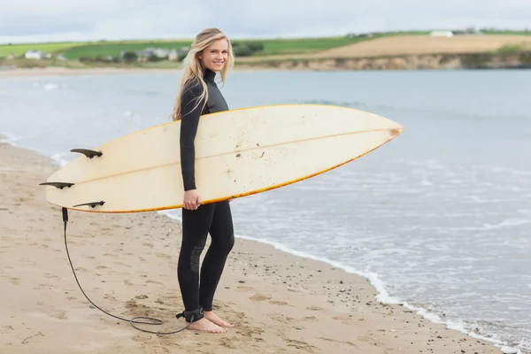 Schöne Frau im Neoprenanzug mit Surfbrett am Strand — Stockfoto