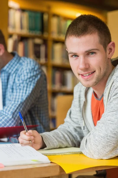 Porträtt av en leende manlig student vid biblioteket skrivbord — Stockfoto