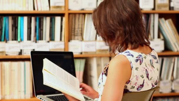 Mujer joven estudiando en la biblioteca con portátil — Vídeo de stock