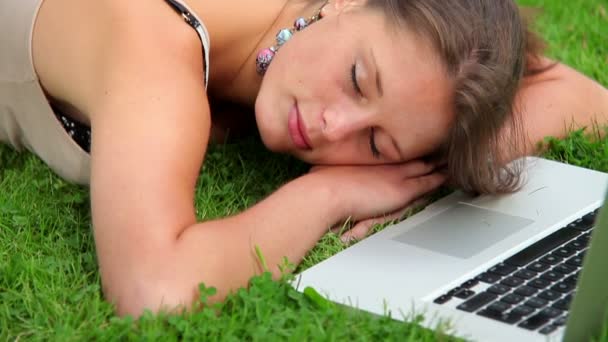 Estudiante feliz durmiendo en la hierba delante de la computadora portátil — Vídeo de stock