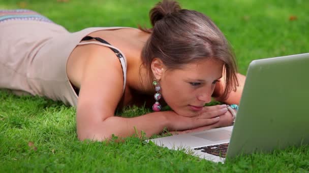 Sonriente estudiante acostado en la hierba mirando a la computadora portátil — Vídeos de Stock