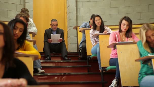 Profesor sentado en los escalones de la sala de conferencias mientras trabaja la clase — Vídeos de Stock