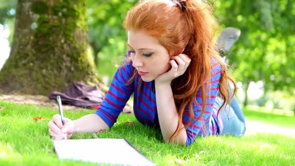 Étudiant couché sur l'herbe prenant des notes — Video